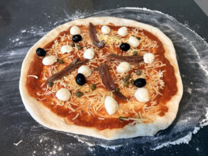 Foto van een vers belegde pizza Romana voordat deze de oven in gaat