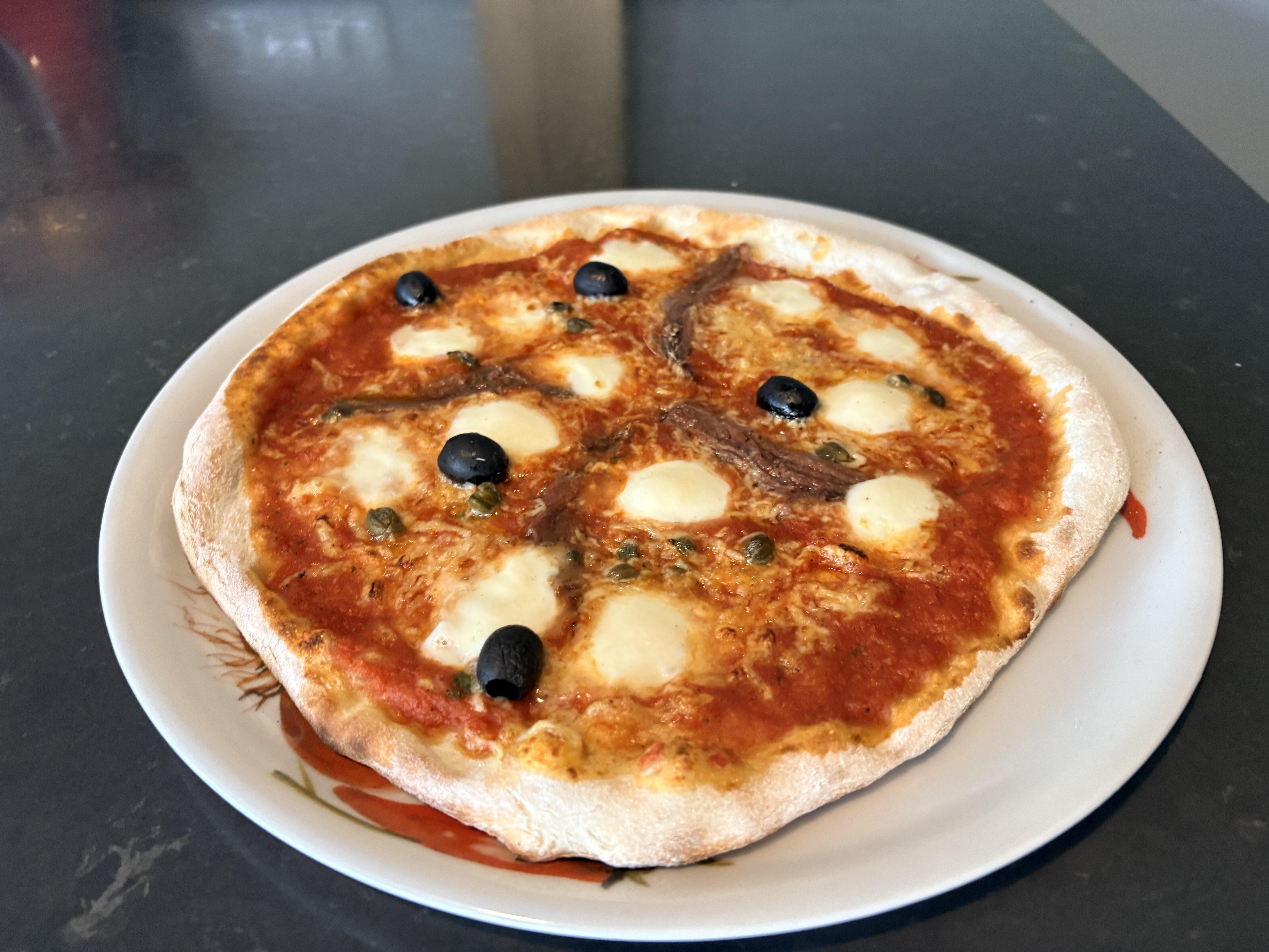 Foto van een versgebakken pizza Romana met mozzarella, ansjovis, kappertjes en olijven